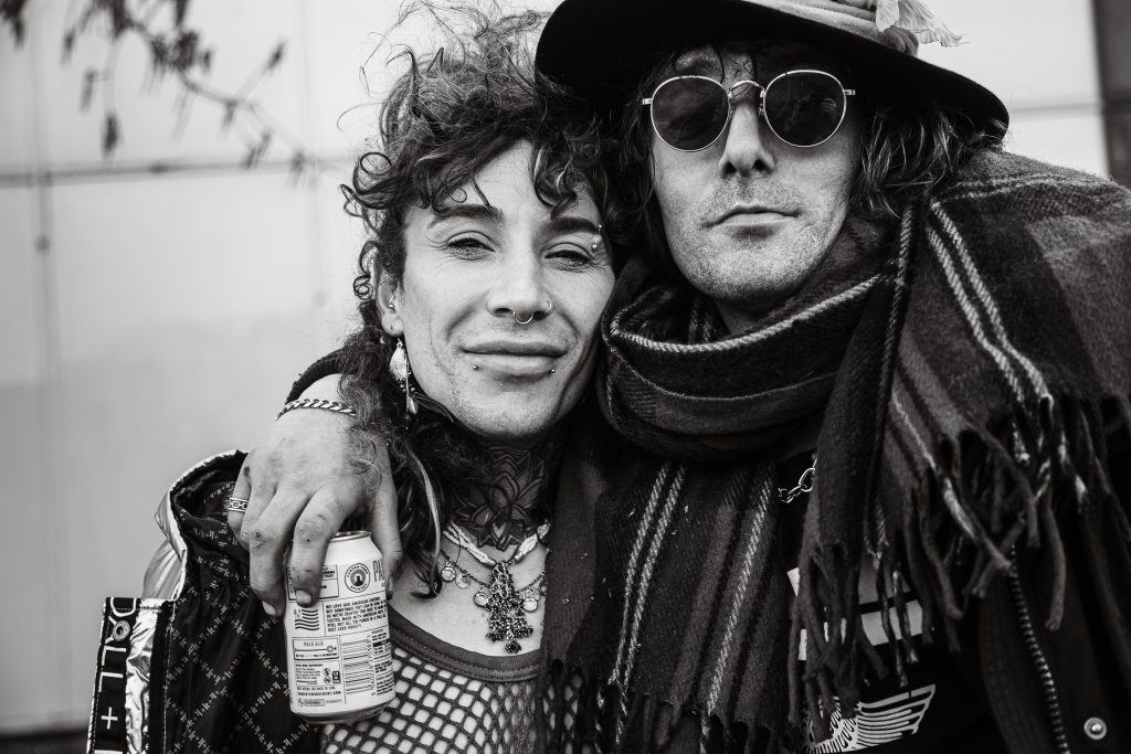 Candid black and white portrait of two figures with distinct style and accessories, captured in a tight embrace.